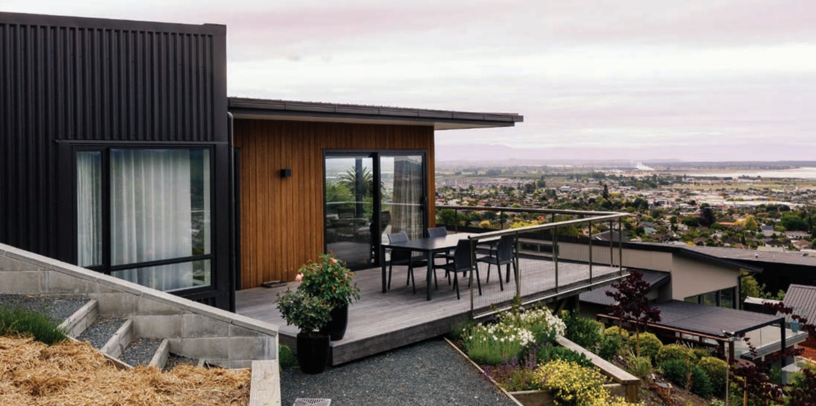 Black-clad hillside house with a cedar wing and a deck looking out over Nelson